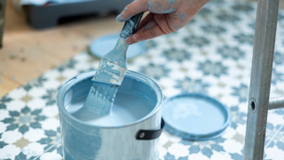 Paint brush dipping in a pot of blue paint