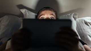 woman looking frightened, watching something on a laptop screen in bed