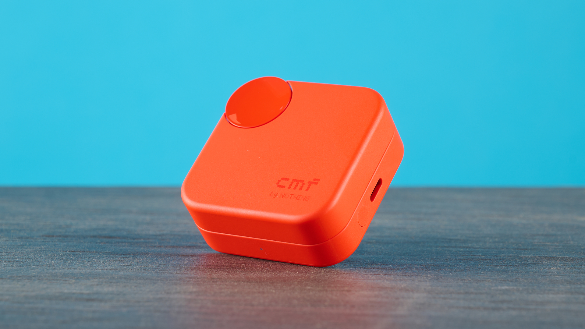 cmf buds 2a in the orange colorway photographed in front of a blue background