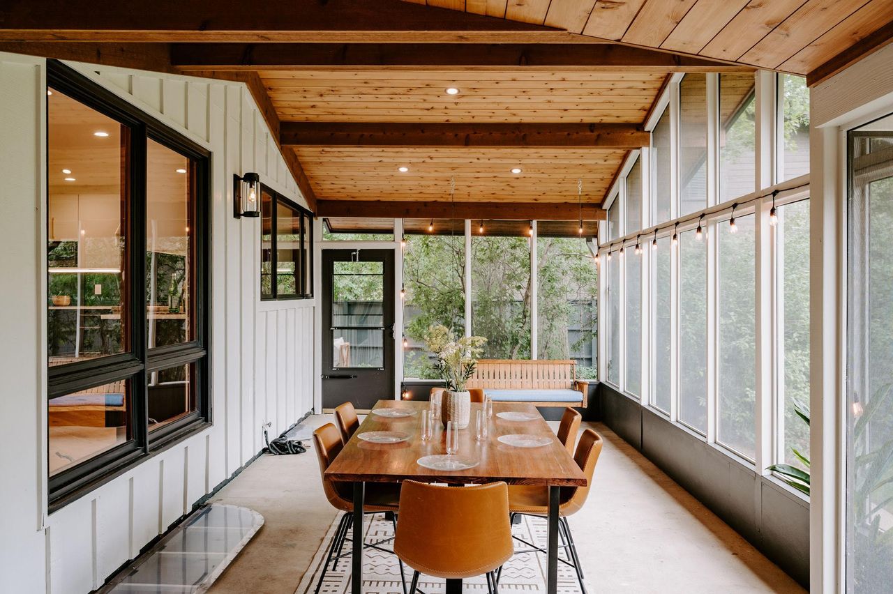 Wooden dining table with chairs in open sunroom/conservatory with a forest view and spot lighting