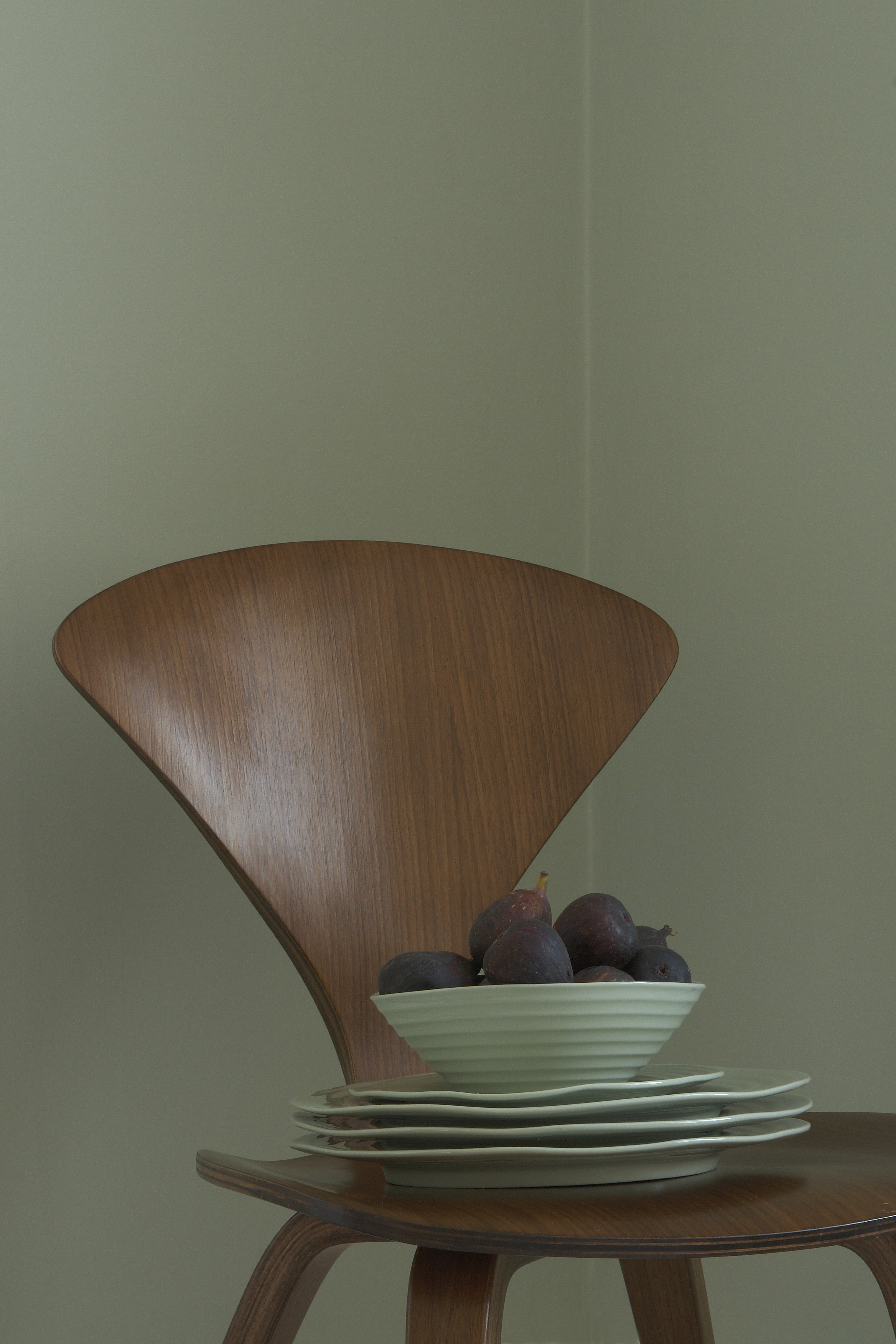 a corner painted in a light green with a wood chair with green plates and figs on
