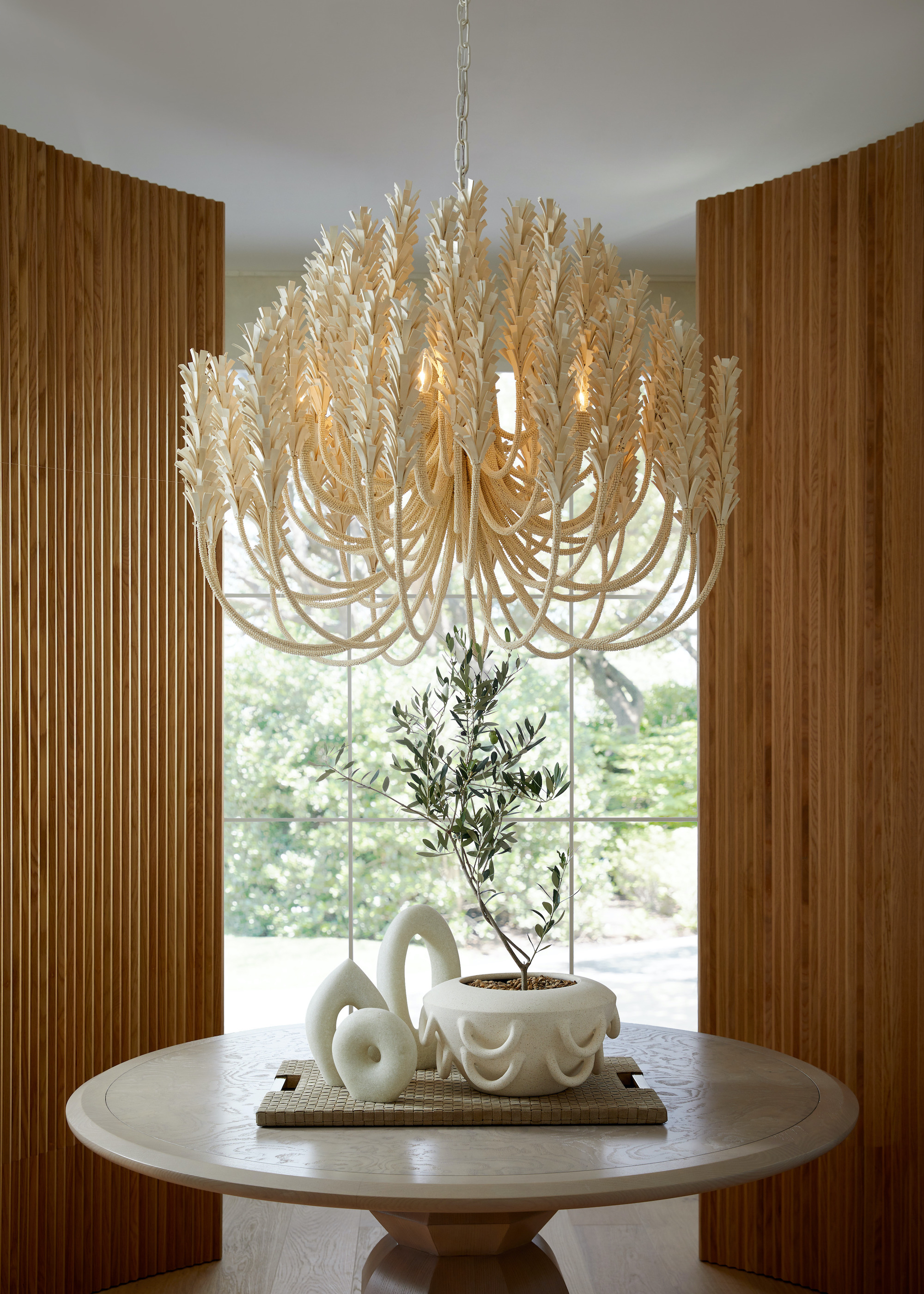 round table with outsized chandelier above the table and on the table is a tray with decorative pieces placed on top