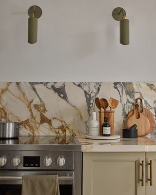 Light green kitchen cabinets with a bold neutral marble splashback and green wall lights