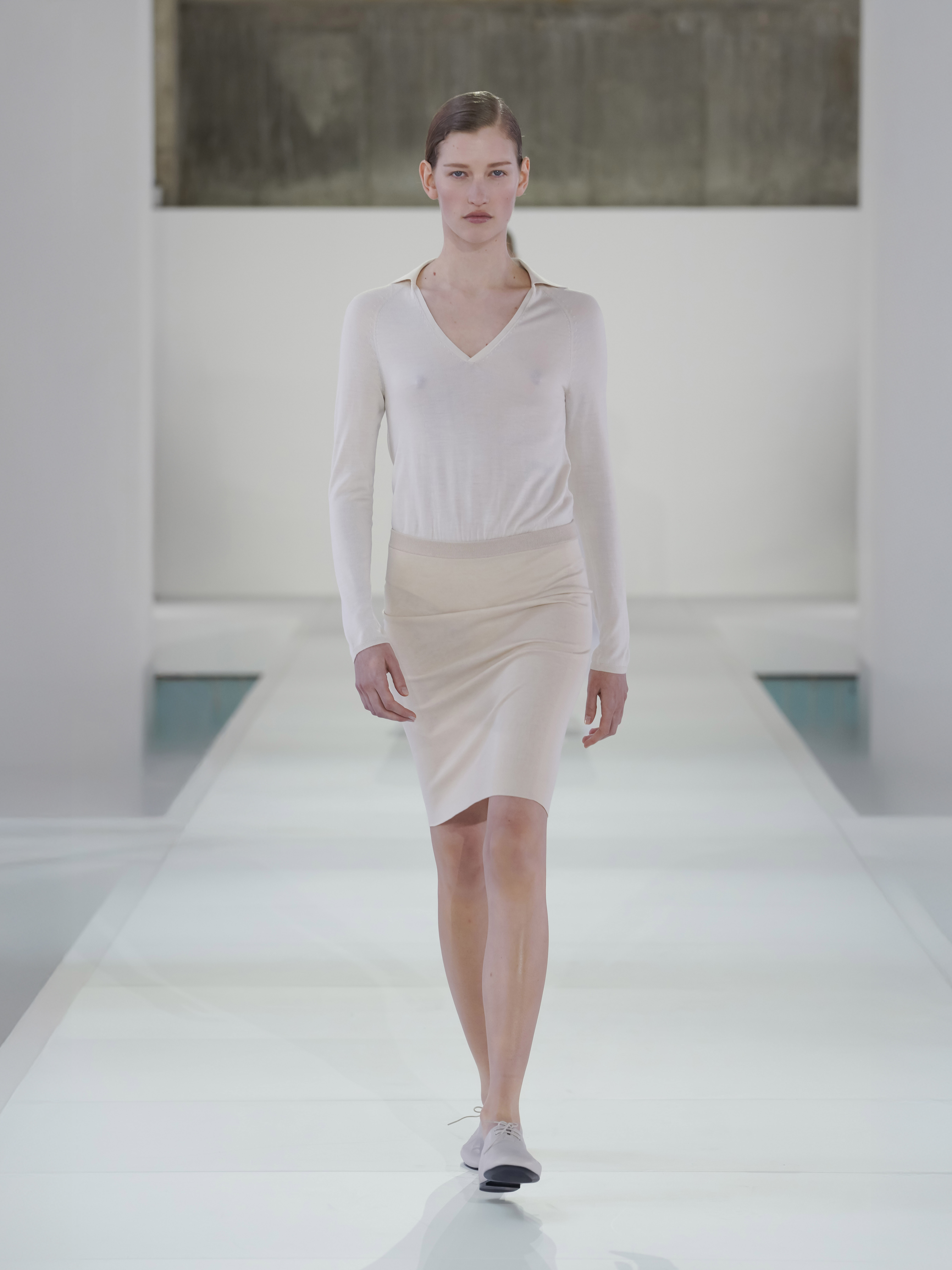 A model walking in the SS26 COS show in Seoul, South Korea, wearing a cream polo-knit top and pencil skirt.
