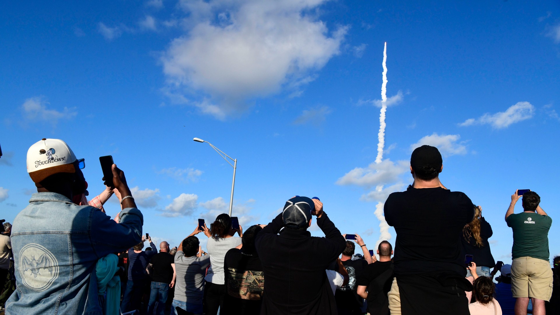 حشد من الناس يوجهون الكاميرات نحو السماء نحو سلسلة من النار والدخان بعيدًا في الخلفية
