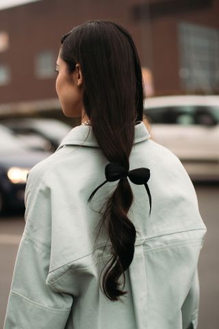 woman with a black bow in a loose ponytail and light blue jacket facing away from the camera