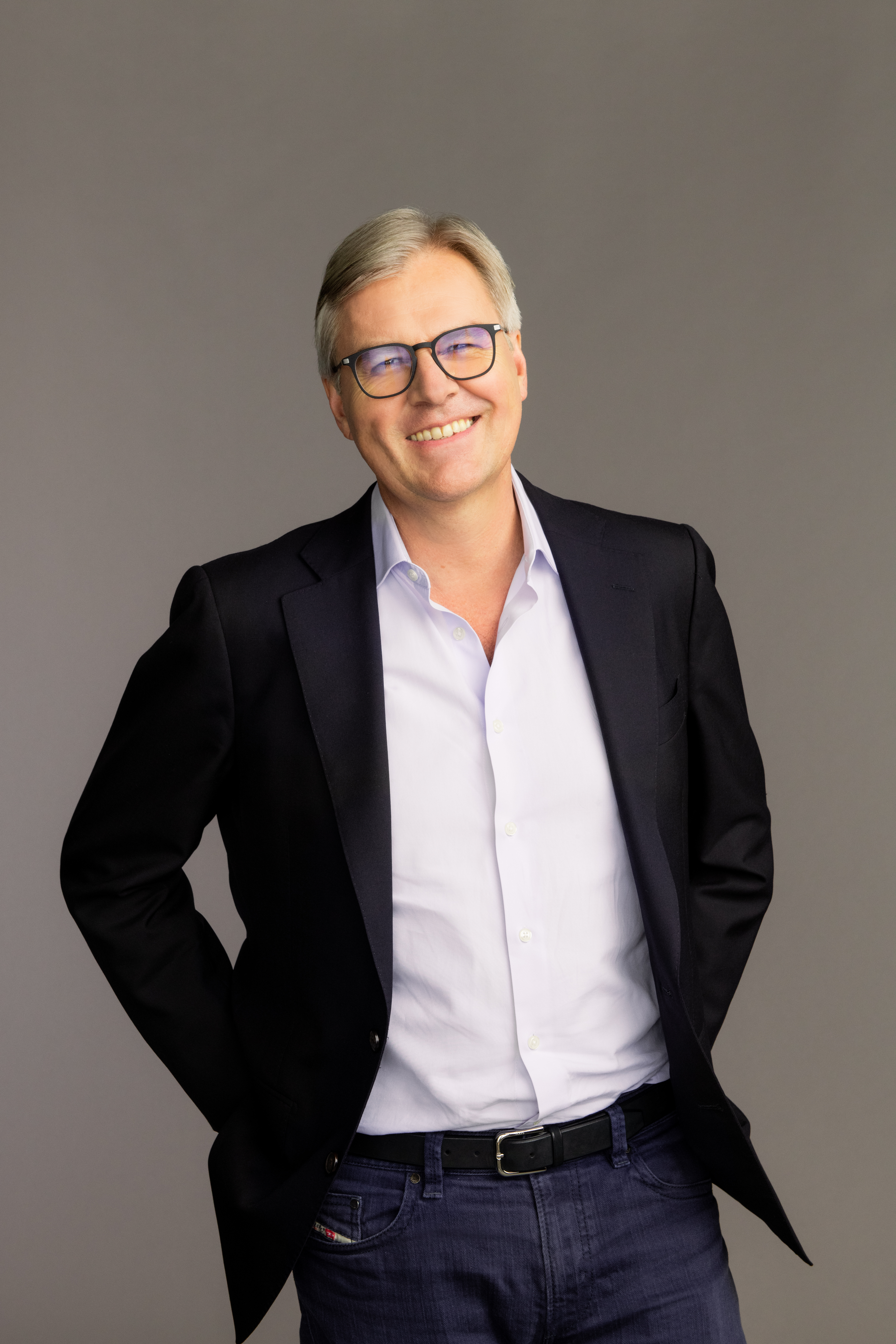 a man with silver hair in a white shirt, black jacket, and jeans