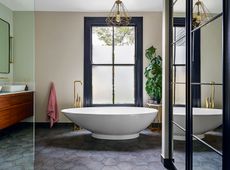 large bathroom with freestanding bath tub, monstera plant, gold faucet and neutral walls