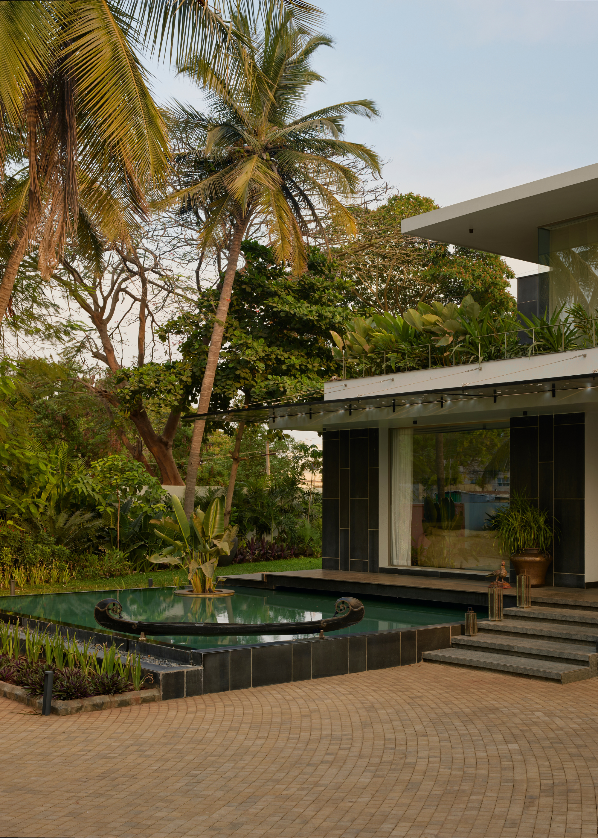 A front yard by a water feature, and lots of plants leading to a stone path and steps up to a home