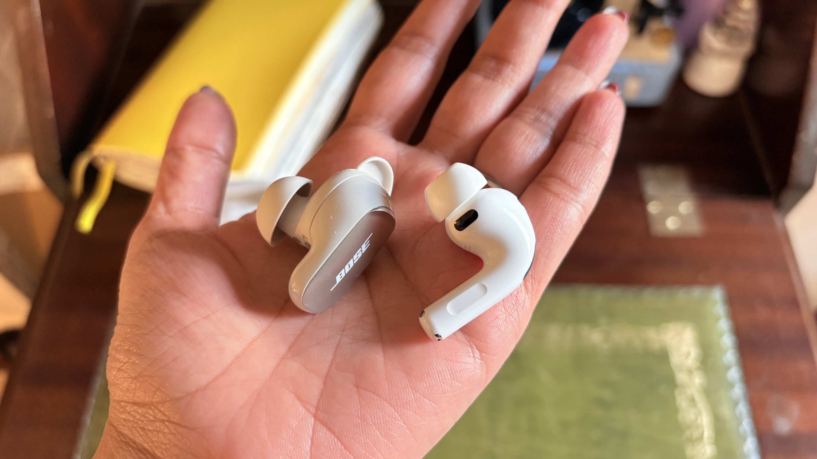 One earbud each of the AirPods Pro 3 and Bose QuietComfort Ultra Earbuds (2nd Gen) held in the palm of a hand.