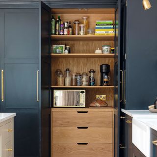 Tall dark kitchen cabinets with gold hardware opening into wooden kitchen pantry