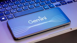 The Google Gemini logo is seen displayed on a smartphone screen next to a laptop keyboard.