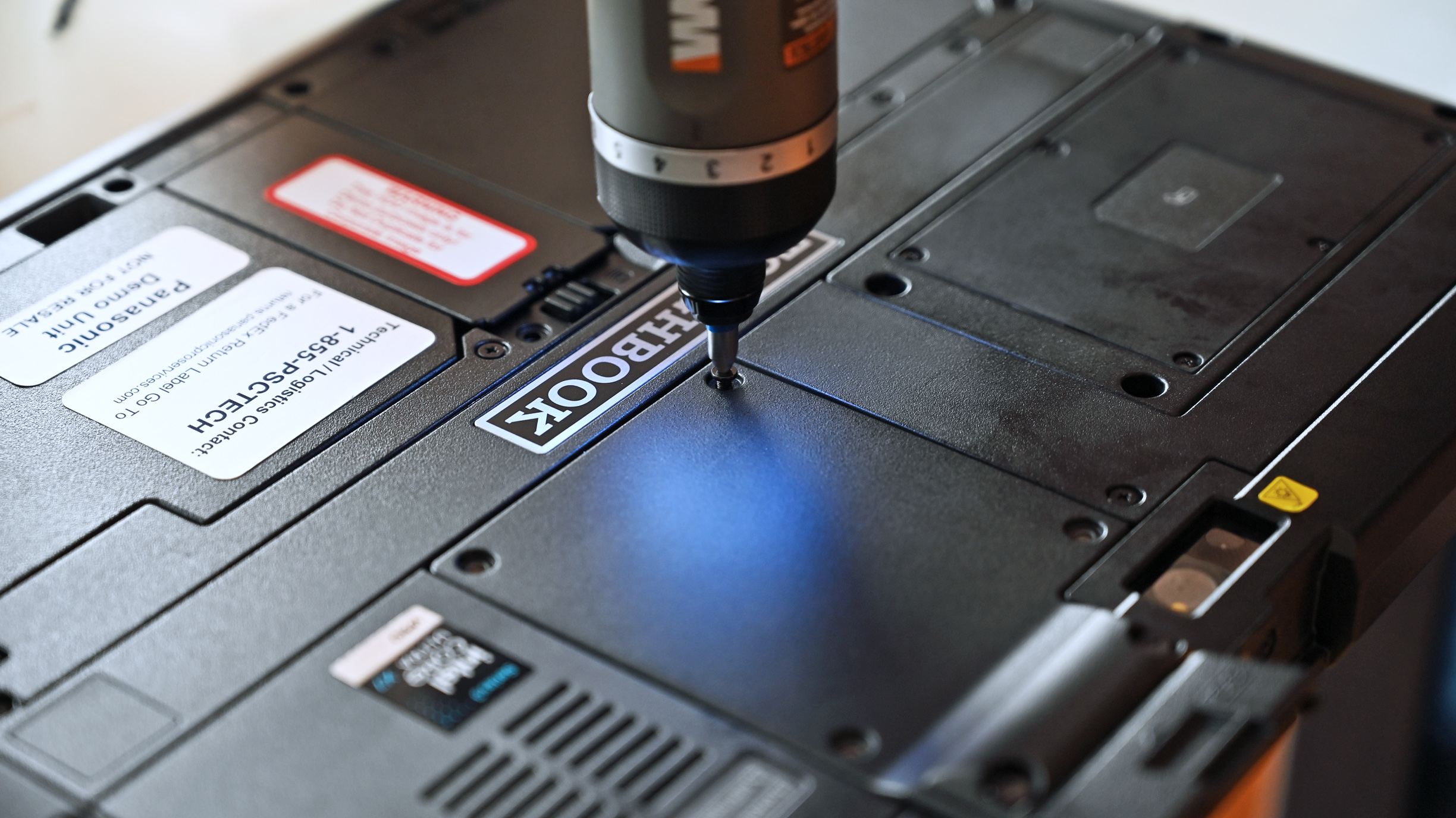 An electric screwdriver tightening a screw into a modular expansion panel on the back of a black Panasonic TOUGHBOOK G3 tablet.