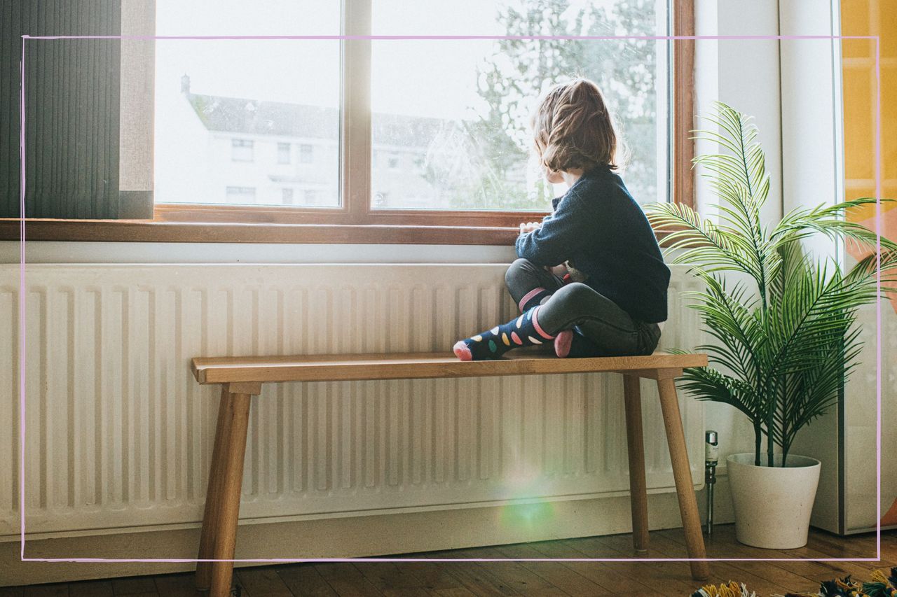 Small child home alone looking out of a window