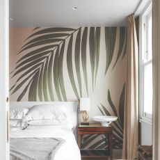 A bedroom with a palm leaf wallpaper, a white bed with matching bedding and ceiling downlights