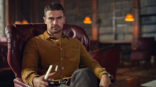 Eddie Horniman (Theo James) sits in a wingback chair for Netflix's "The Gentlemen"