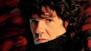 Gary Moore posing for a photograph against a red backdrop