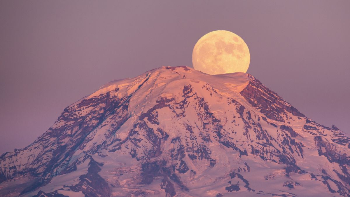 full moon rising behind a snowcapped mountain.