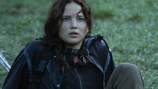 Jennifer Lawrence as Katniss Everdeen looking scared while sitting down on grass in The Hunger Games