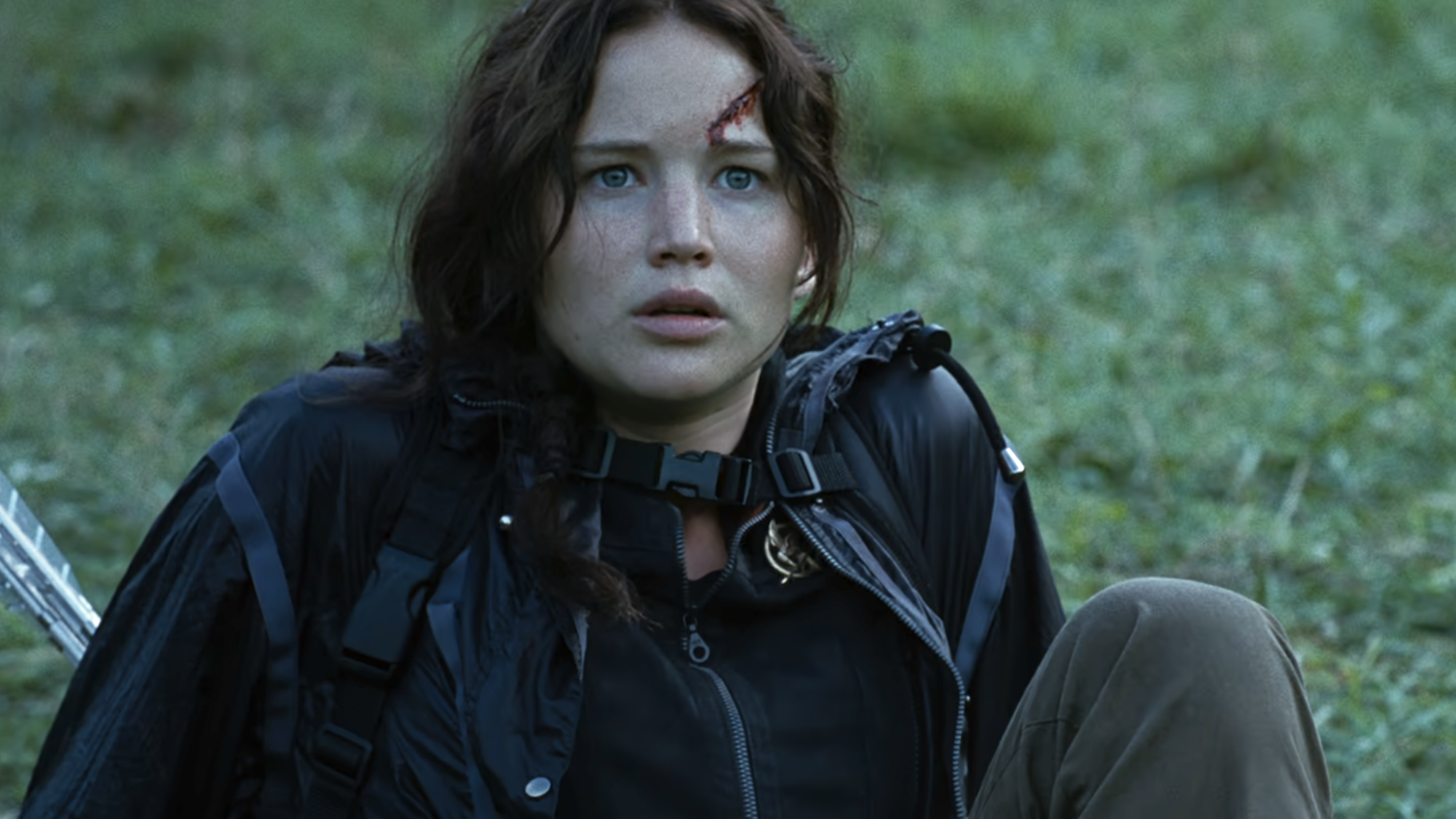 Jennifer Lawrence as Katniss Everdeen looking scared while sitting down on grass in The Hunger Games