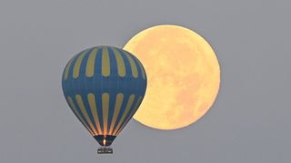 a close up of one blue hot air balloon and the full moon.