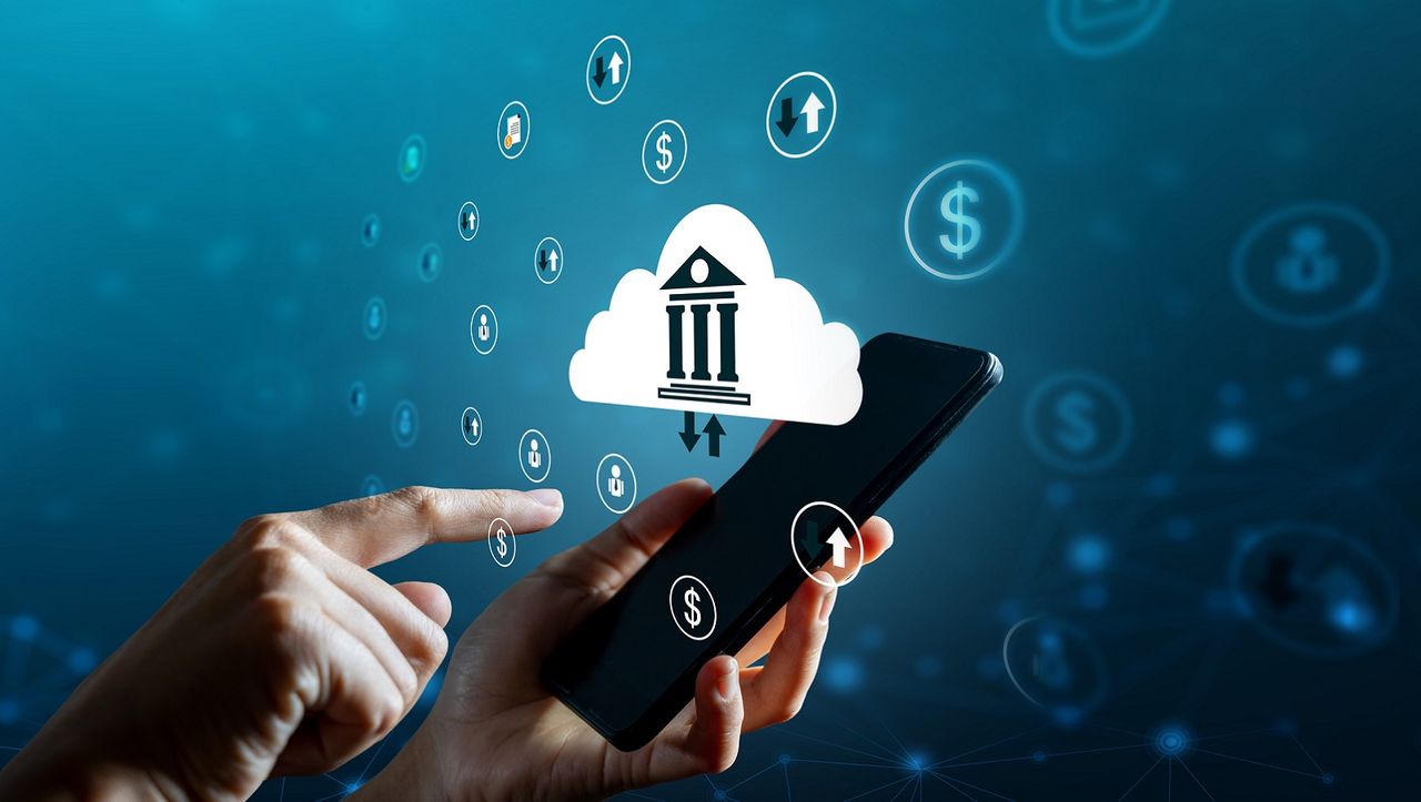 Bank symbol in a cloud symbol as someone does an online transaction on a smartphone.