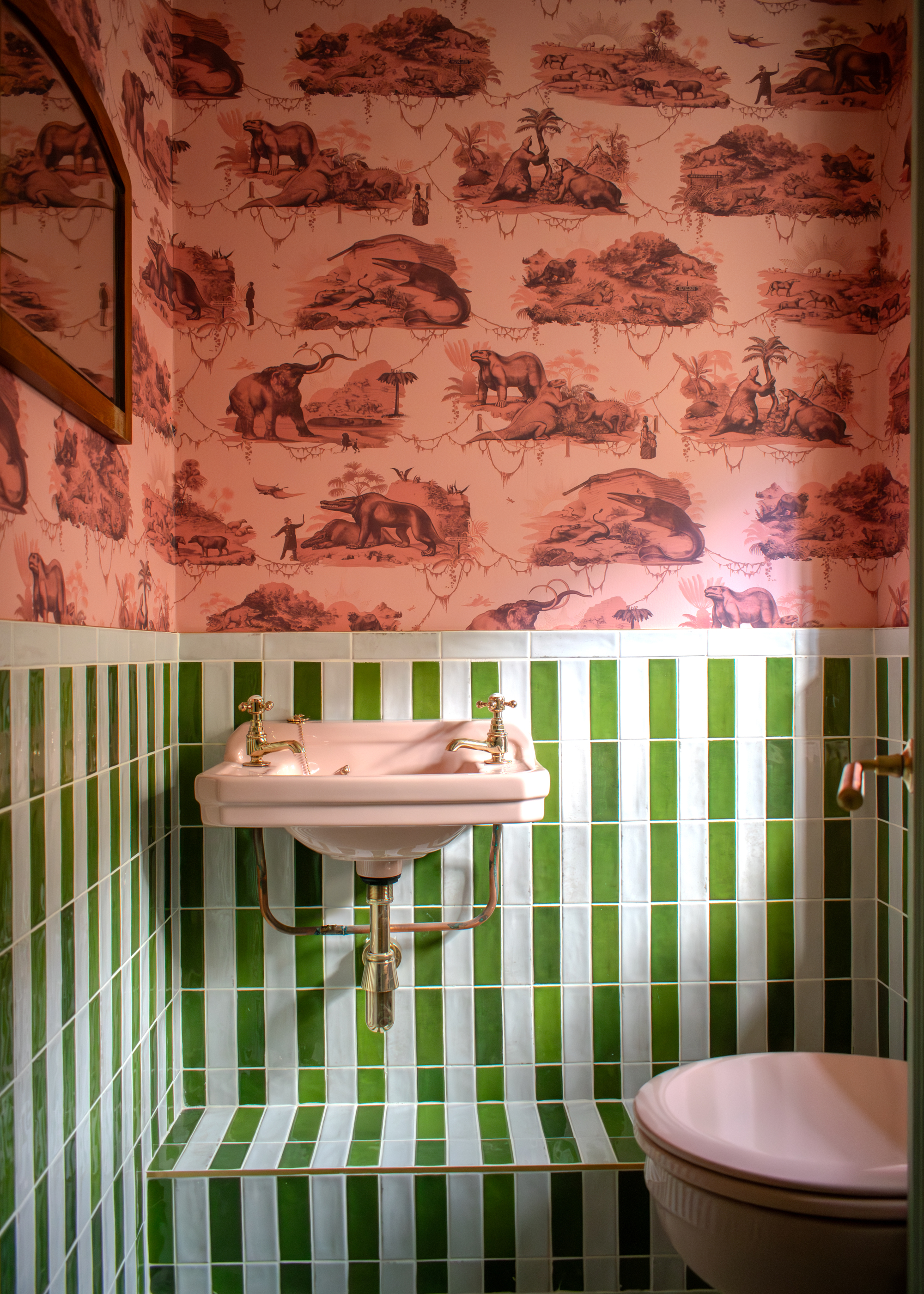 A powder room with green and white striped tiles and pink patterned wallpaper on the upper portion of the walls