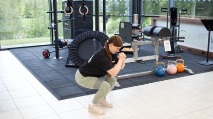 Personal trainer from Fitness Superstore demonstrates a squat with the aid of a resistance band