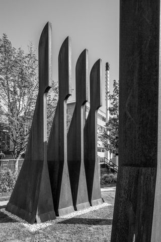 A black & white photo of a steel sculpture. Tall and narrow triangle-like shape structure, with a hook-like top.