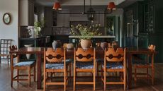 a dining area with vintage swedish pine chairs looking through to an open plan dark green kitchen