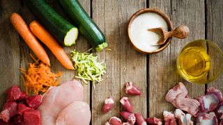 Homemade dog food recipes: a selection of ingredients including carrots, courgette, chicken and beef on a wooden surface