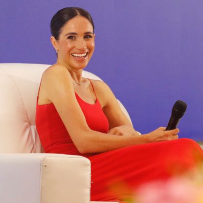 Meghan Markle wears a red dress with thin straps by Orire while onstage at a Women in Leadership panel