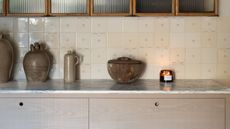 Small kitchen countertop in marble, with deVOL Kitchen Ditsy Delft wall tiles. These are small, varied shades of cream with tiny floral design in center of some of the tiles, not all. Ceramic pots can be seen on the counter, as well as the top drawers