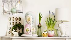 Easter decorations including eggs, rabbit lamb, grape hyacinths and bulbs in vases and tea cups on a console table