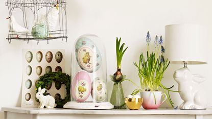 Easter decorations including eggs, rabbit lamb, grape hyacinths and bulbs in vases and tea cups on a console table