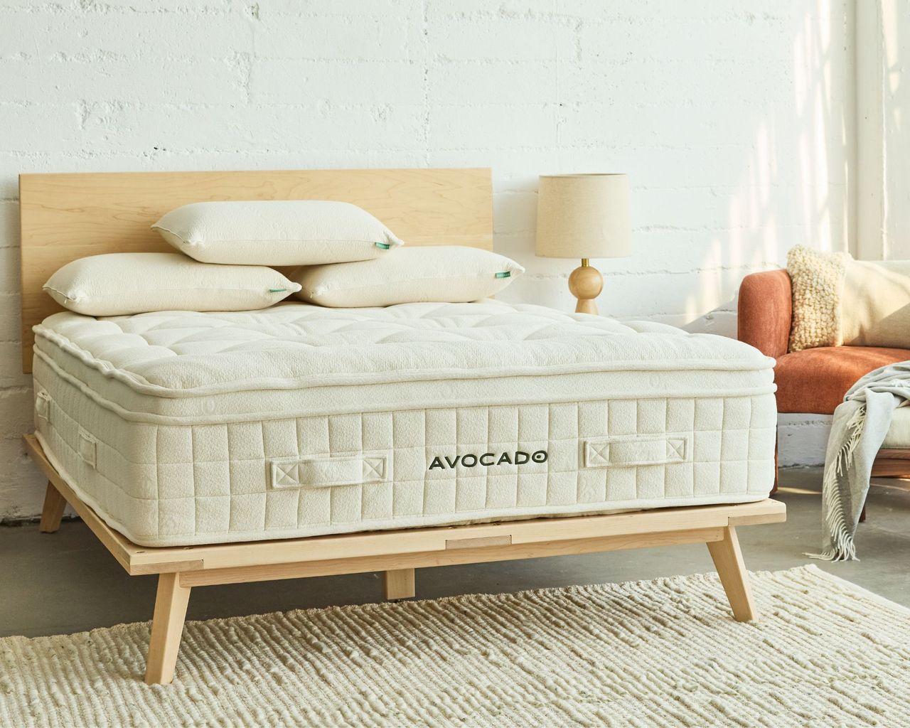 Avocado Luxury Organic Mattress in a white bedroom on a light wood bedframe with three pillows and a white rug