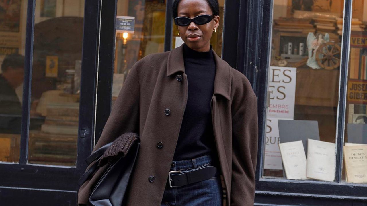 woman standing in front of doorway with brown leather jacket, black turtleneck, and denim skirt