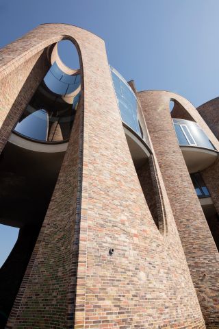 Fjordenhus, by Olafur Eliasson and Studio Olafur Eliasson in Vejle, Denmark. Upward view of a face brick two storey building with triangular arched windows.