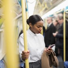 UK, London, businesswoman in underground train looking at cell phone