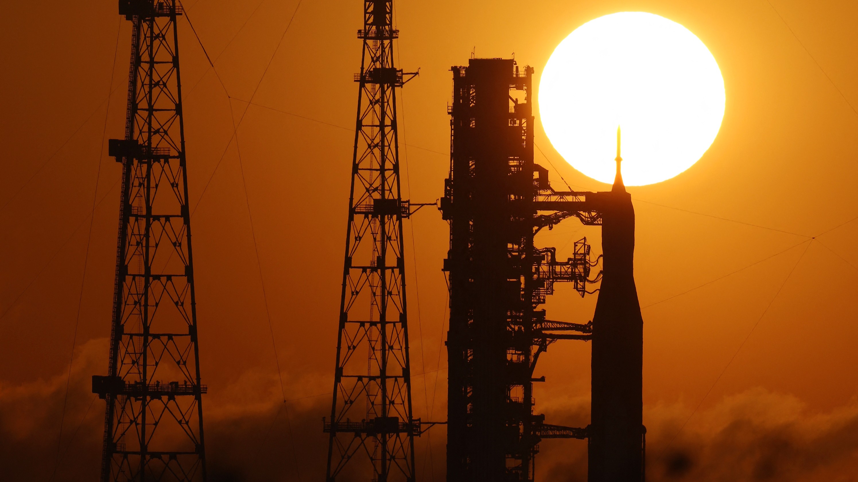 A photo of the sun rising above the Artemis II Space Launch System rocket and Orion spacecraft at Kennedy Space Center in Florida. 