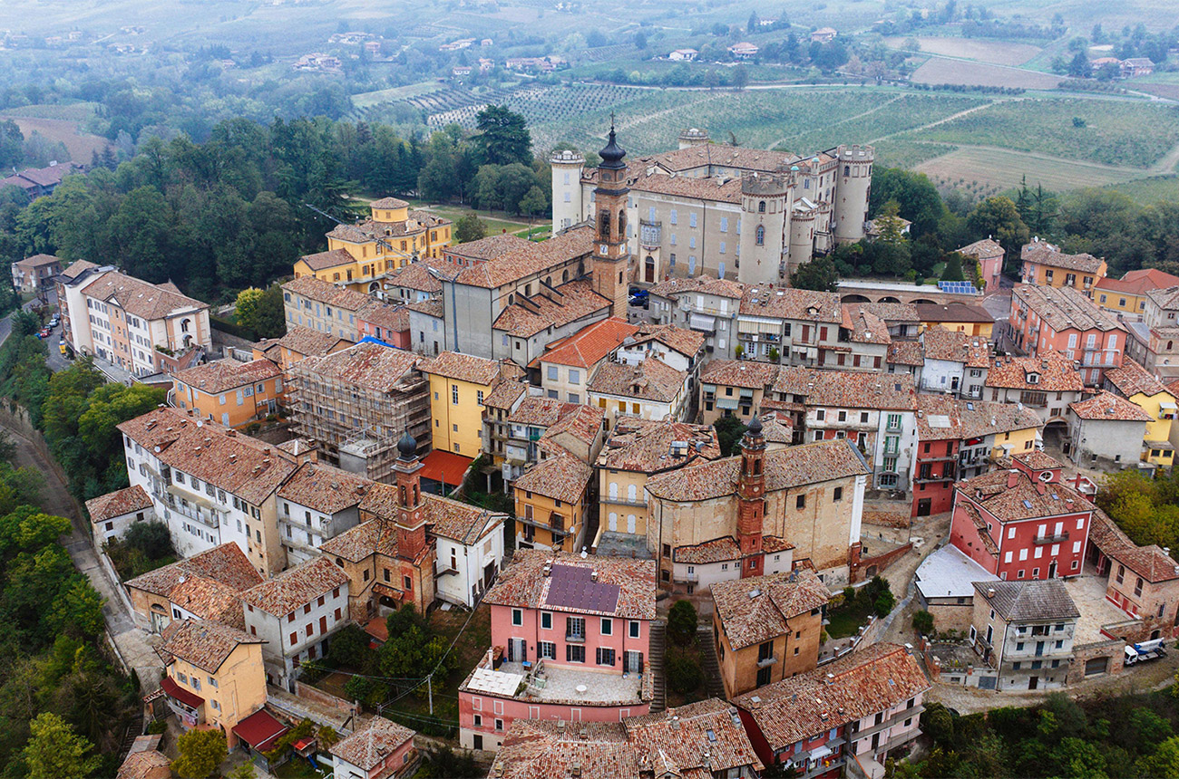 Birds-eye view of a little town with different coloured house and a large church, surrounded by green fields