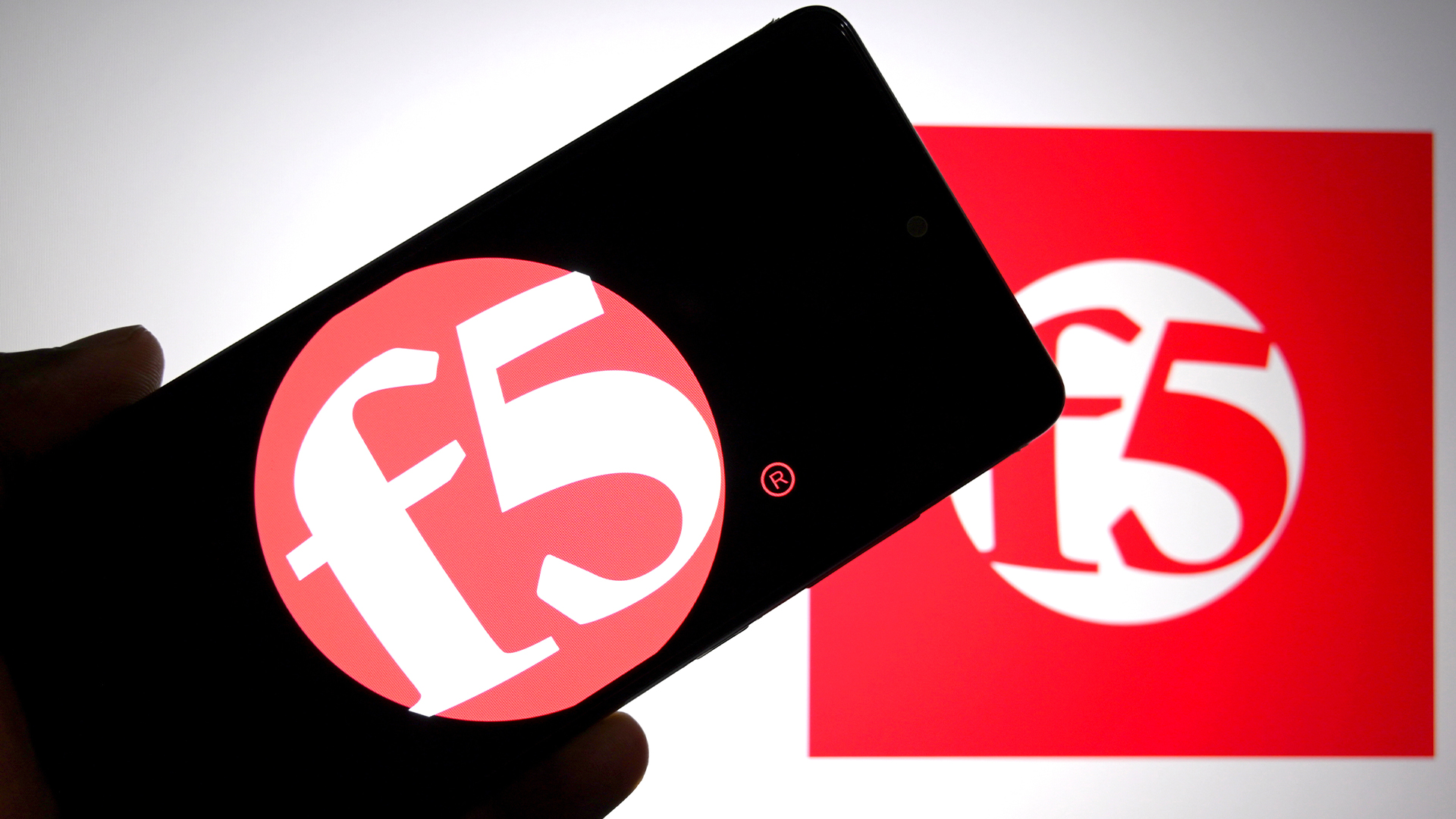 F5 logo and branding pictured on a smartphone screen held up in hand with company logo in background.