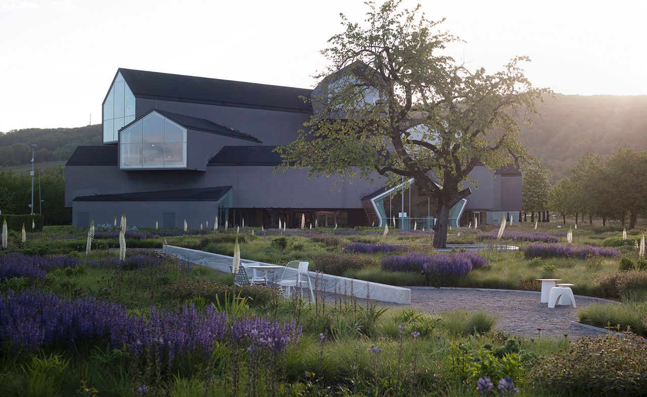 Vitra Haus, a multi-storey building part of the Vitra Campus in Weil am Rhein, Germany, photographed at sunset among greenery and purple flowers, part of Piet Oudolf&#039;s garden design