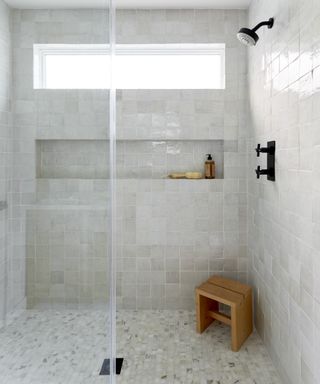 A shower with small calacatta marble tiling on the floor and white zellige tiles on the walls