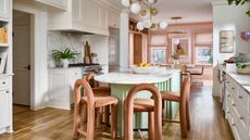Image of a large white kitchen with a mint green kitchen island that has dark orange chairs around it. There is a light pink dining room in the background.
