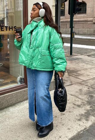 a roundup of the best puffer jackets shown in a photo of a woman wearing a green puffer coat with a denim maxi skirt and knee-high black boots