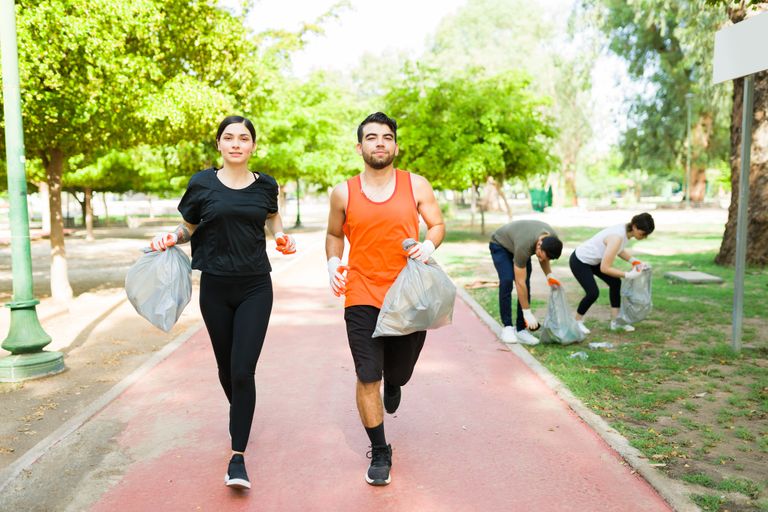 Attractive latin couple holding trash bags with garbage while running. Group of friends doing plogging in the park
