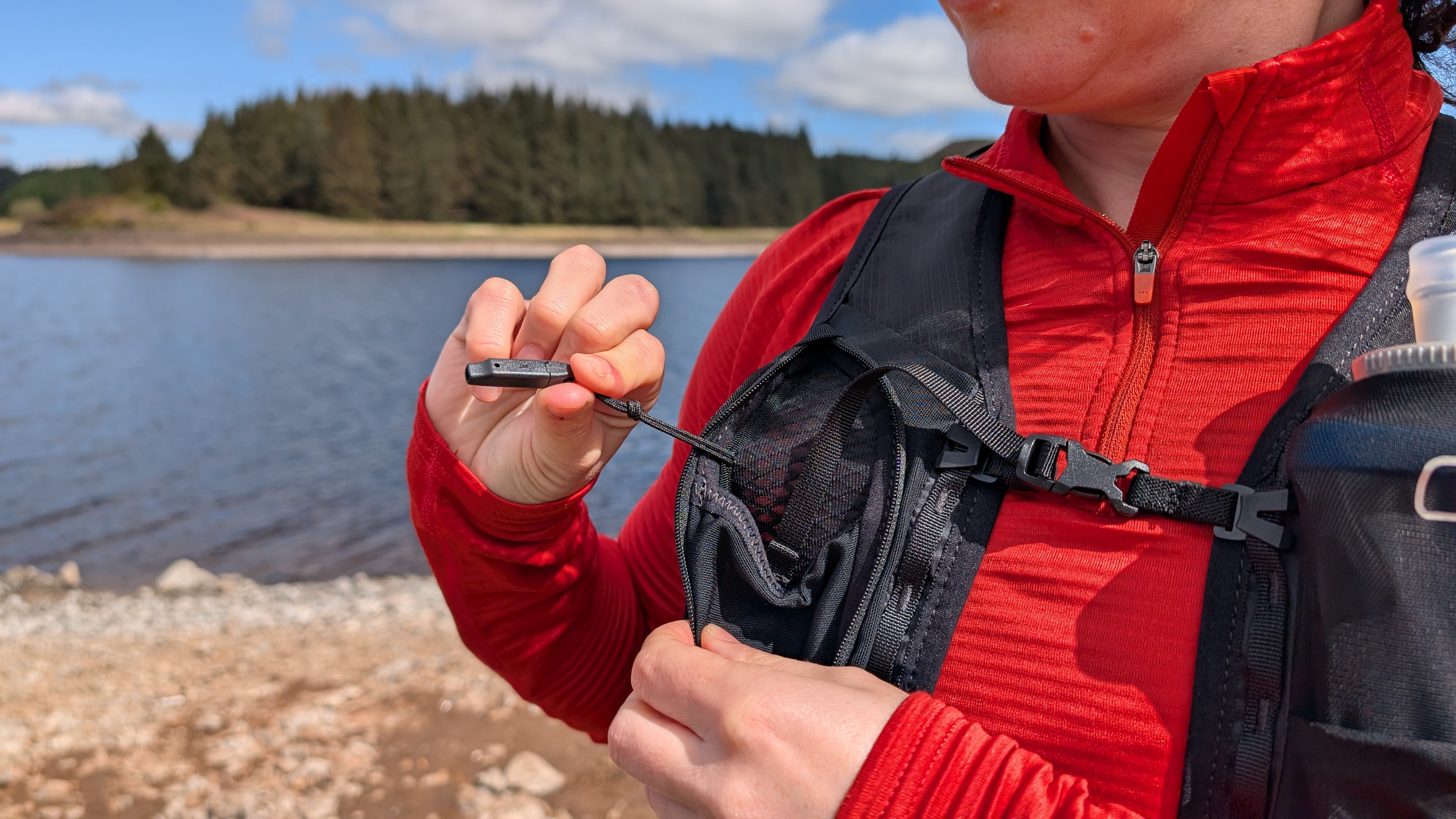 A woman hiker pulls out the emergency whistle from a blue Berghaus Fasthike F15 backpack