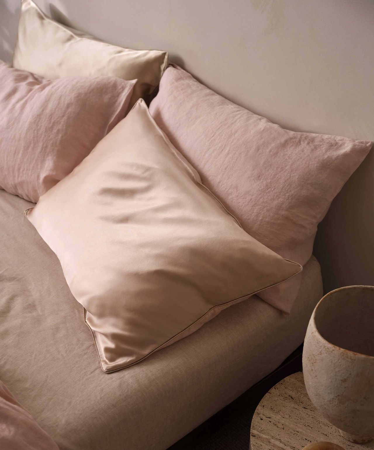 Close-up image of a bed that has four pillows made of silk and linen and in a blush pink color.