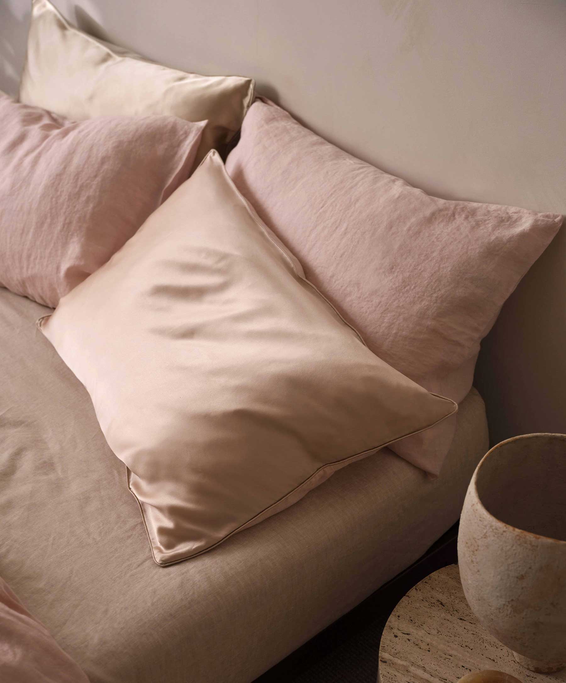 Close-up image of a bed that has four pillows made of silk and linen and in a blush pink color.
